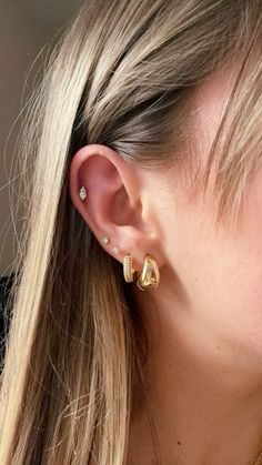 a woman with long blonde hair wearing two gold ear piercings on her left ear