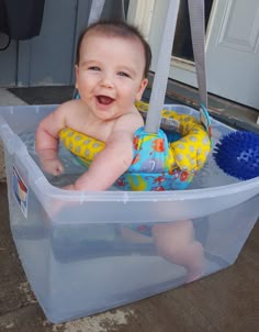 a baby sitting in a plastic tub with a blue brush and toy on it's back