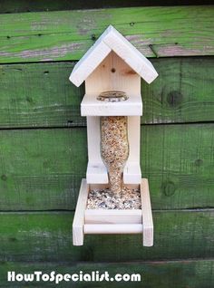 a bird feeder hanging from the side of a green wooden wall