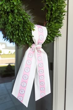 a pink and white ribbon hanging from a door with a green wreath on the front