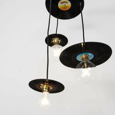 three black vinyl records hanging from the ceiling with light bulbs in between them and an old record on top