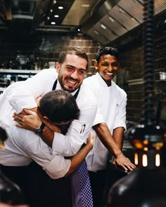 two men hugging each other while standing in front of a kitchen counter with chefs behind them