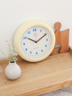 a white clock sitting on top of a wooden table next to a vase with flowers