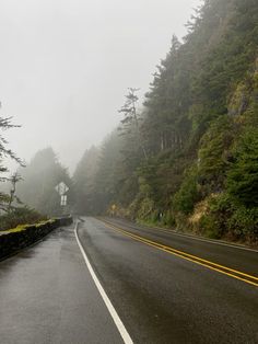 an empty road in the mountains with trees on both sides and foggy skies above