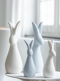 three white and one blue ceramic rabbits sitting on a table in front of a window