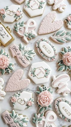 wedding cookies are arranged on a table with pink flowers and monogrammed names in the middle