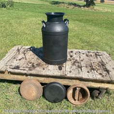 a large black vase sitting on top of a wooden pallet next to other pots and pans