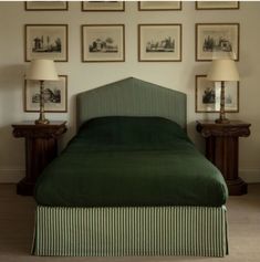 a bed with green bedspread and two lamps in front of pictures on the wall