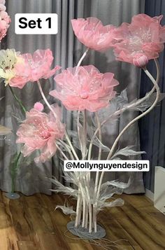 pink and white flowers in a clear vase on a wooden floor next to a curtain