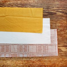 two pieces of fabric sitting next to each other on top of a wooden table, one yellow and the other white