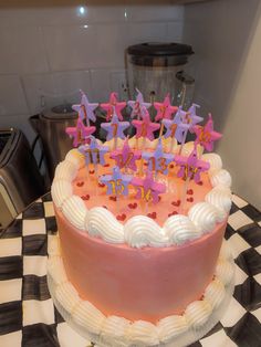 a birthday cake with pink frosting and purple stars on top is sitting on a checkered tablecloth