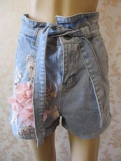 "Stone washed light denim shorts with pink embroidery and pink appliqued flowers on the front.  They have a high waist with a tie belt,  turned up hem, a zip fly and 2 pockets front and back. Waist flat;  30\" Outside leg from waist;  25\" Width of leg;  12\" Made by REAULAR cotton denim" Floral Print Shorts For Spring, High Waist Jeans For Summer Festival, Summer Festival High Waist Jeans, Cute Denim Bottoms For Summer, High Waist Jean Shorts For Summer, Trendy Jean Shorts For Spring Festival, Cute Summer Denim Bottoms, Bohemian Shorts For Spring, Spring Bohemian Shorts