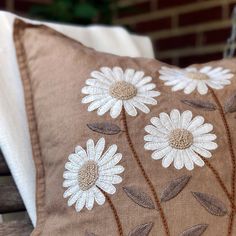 a brown pillow with white daisies on it sitting on a wooden bench next to a brick wall