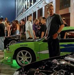 a man standing next to a green sports car in front of other people on the street