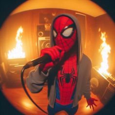 a man in a spiderman costume singing into a microphone with flames behind his head