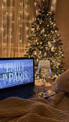 an open laptop computer sitting on top of a bed next to a christmas tree with lights