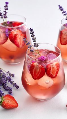 three glasses filled with liquid and strawberries on top of a white table next to lavender sprigs