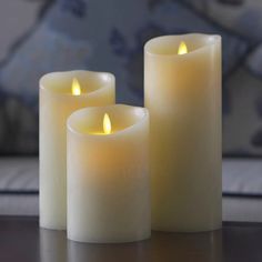 three white candles sitting on top of a wooden table next to each other with one candle lit