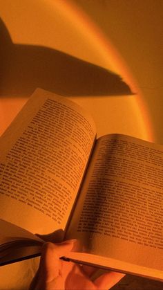 an open book in someone's hand with the light shining on them and their shadow