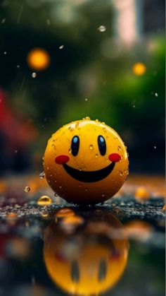 a yellow smiley face ball sitting on top of a wet surface with water droplets around it