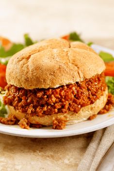 a sloppy joe sandwich on a plate with lettuce and carrots in the background