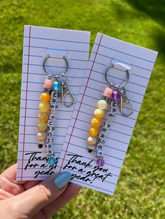 two key chains with beads on them are being held in front of a notepad