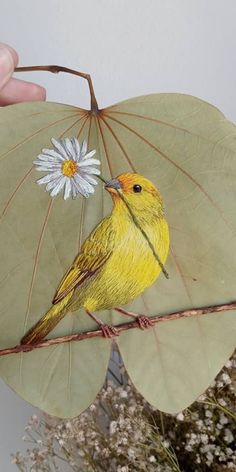 a yellow bird sitting on top of a green leaf next to a white and gray flower