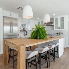 a kitchen with a wooden table surrounded by white stools and plants on the island