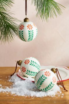 three ornaments hanging from a pine tree on top of snow covered plates and spoons