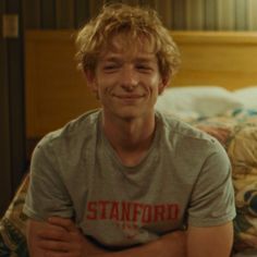 a smiling young man sitting on top of a bed