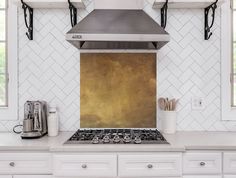 a stove top oven sitting inside of a kitchen next to white cupboards and windows