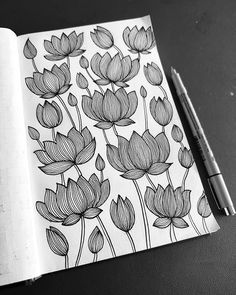 an open notebook with black and white flowers drawn on the pages next to a pen