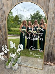 three women standing in front of a mirror with the words welcome to our wedding written on it