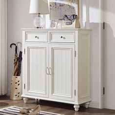 a white cabinet sitting on top of a hard wood floor next to a lamp and rug