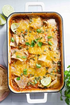 mexican chicken enchilada casserole in a white baking dish with limes and cilantro on the side