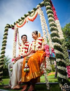 a man and woman sitting on top of a bench next to each other in front of flowers