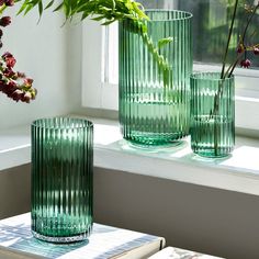 three green vases sitting on top of a window sill next to a plant