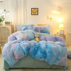 a bed covered in blue and purple fluffy fur with a smiley face on the pillow