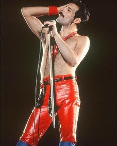 a man in red leather pants holding a microphone and singing into the air with his hands behind his head