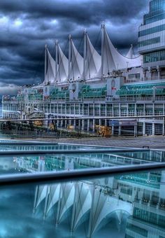 a large building with many windows next to the water and clouds in the sky above it