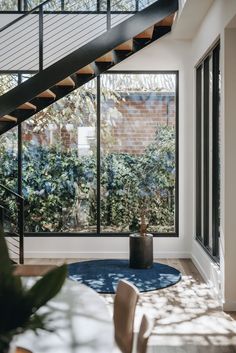 a living room filled with furniture and lots of windows next to a stair case in front of a brick wall