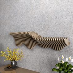 a vase with flowers on a table next to a wall mounted wooden object that is shaped like a fish