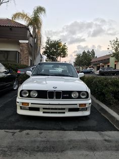 a white car is parked in the parking lot next to some bushes and cars on the street