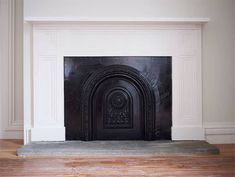 an empty fireplace in a white room with wood flooring and moldings on the mantle