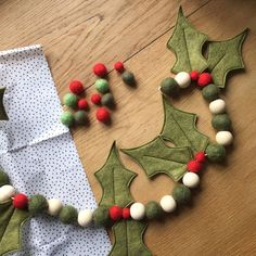 felt holly decorations are laid out on the floor next to a piece of fabric with pom - poms