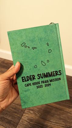 a person holding up a green book that says elder summers cape verde prairie mission 2012 - 2014