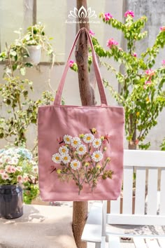 a pink tote bag with daisies on it hanging from a wooden tree branch