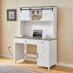 a computer desk with a laptop on top of it in front of a beige wall