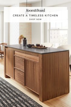 a kitchen island with black granite top and wooden cabinetry in front of large windows