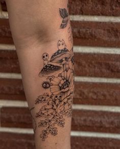 a woman's leg with flowers and mushrooms tattoo on her left calf area, along with an owl sitting on the mushroom